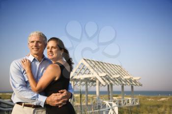 Attractive couple embrace on the beach with arbor in background. Horizontal shot.