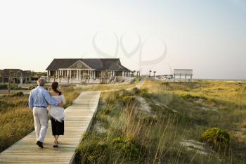 Couple walk on the boardwalk towards a beach pavilion. Horizontal shot.