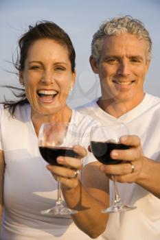 Closeup of a happy couple as they raise their glasses of red wine to the camera. Vertical shot.