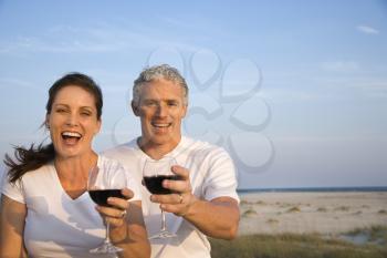 Happy couple drink wine on the beach and raise their glasses to the camera. Horizontal shot.