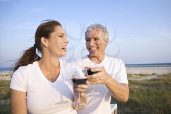 Couple laugh and drink wine on beach. Horizontal shot.