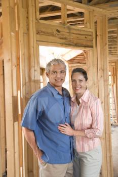 Smiling couple stand together inside their partially built home. Vertical shot.