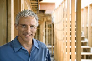 Man stands inside a partially constructed home and smiles towards the camera. Horizontal shot.