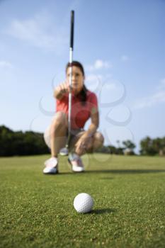 Closeup of a golf-ball with a woman lining up her putt in the background. Vertical shot.