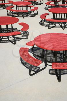 Red metal circular cafeteria tables on an outdoor patio. Vertical shot.