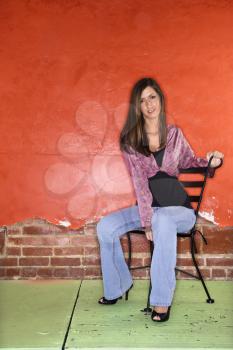 Attractive young adult woman sitting on a chair in front of a colorful wall. Vertical shot.