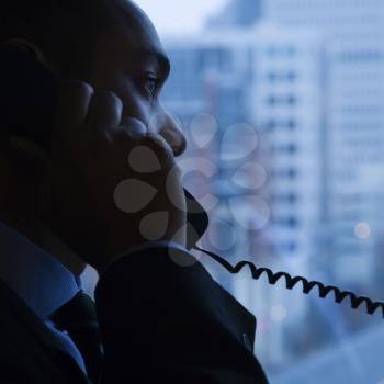 Side view of an African-American businessman speaking over the telephone. A window with a city view is in the background. Square shot.