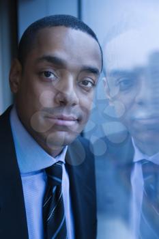 African-American businessman smiles towards the camera. His reflection can be seen in the window. Vertical shot.