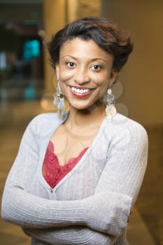 Attractive young African-American woman stands and smiles at the camera with crossed arms. Vertical shot.