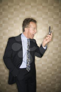 Caucasian middle-aged businessman holds a phone away from his face as he yells into it. Vertical shot.