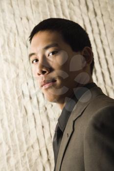 Low angle head-and-shoulders portrait of Asian young adult businessman. Vertical format.