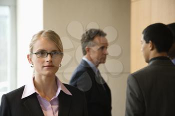 Caucasian mid-adult business woman in foreground with group of businessmen in the background. Horizontal format.