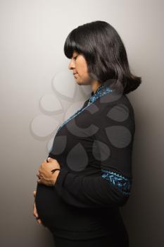 Profile portrait pregnant woman with her hands on her belly. Vertical shot. Isolated on gray.