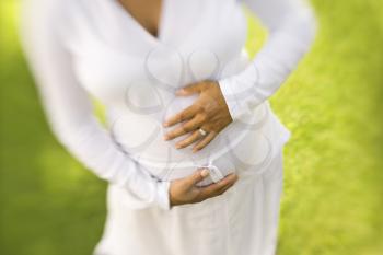 High angle view of the torso of a pregnant woman with her hands on her belly. Horizontal shot.