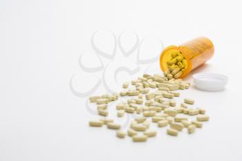 Yellow pill bottle with brown tablets spilling out onto a white surface. Horizontal shot. Isolated on white.