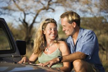 A man and woman smile at each other as they share a map spread out on the hood of a car. Horizontal format.