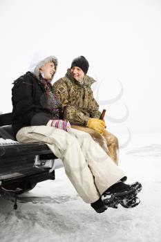 Young adult man and woman drinking beer and sitting on the tailgate of a truck in a winter environment. Vertical shot.