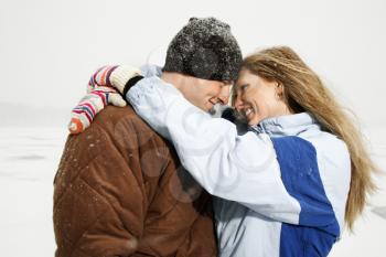 Young adult couple smiling at each other and in a close embrace in a winter environment. Horizontal shot.