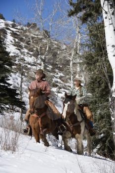 Man and young woman riding horses up a snowy hill on a country landscape Vertical shot.