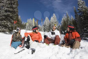 Group of male and female skiers sitting in the snow relaxing talking and smiling. Horizontal shot.