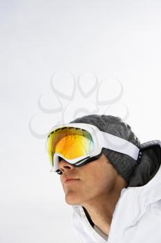 Head shot of a male skier wearing ski goggles against a snowy white background. Vertical shot.