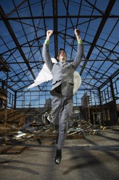 Young businessman with angel wing attempts takeoff in abandoned building. Vertical shot.