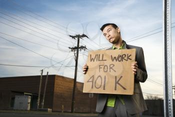 Young businessman stands on a street corner holding a sign that reads 'will work for 401 K'. Horizontal shot.