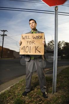 Young businessman stands on a street corner, holding a sign that reads 'will work for 401 K'. Vertical shot.