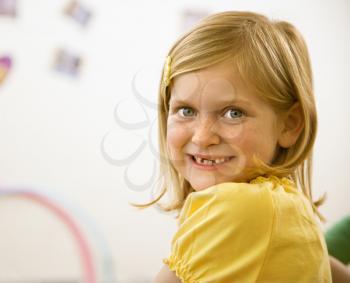 Young blond girl smiling over shoulder at viewer. Vertically framed shot.