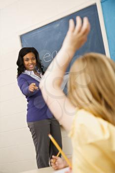 Teacher smiling and pointing to student with hand raised. Vertically framed shot.