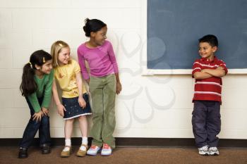 Students standing in classroom. A boy is separate from the girls. Horizontally framed shot.