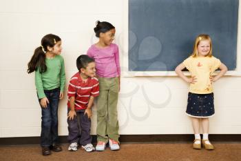 Students standing in classroom. A girl is separate from the group. Horizontally framed shot.