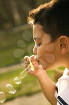 Young boy blowing bubbles outside. Vertically framed shot.