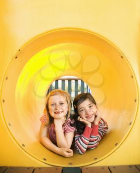 Young girls lying together in crawl tube at playground. Vertically framed shot.