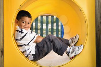Young boy lying in crawl tube at playground. Horizontally framed shot.