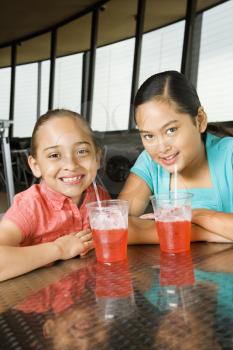 Hispanic and Asian girls seated at a table with drinks smiling for the viewer. Vertical shot.