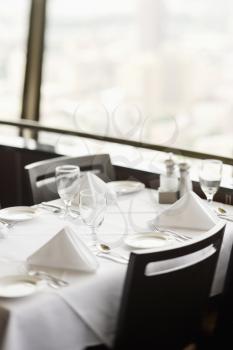 High angle view of a restaurant table with place settings and a white tablecloth.  The table is by a window. Vertical shot.