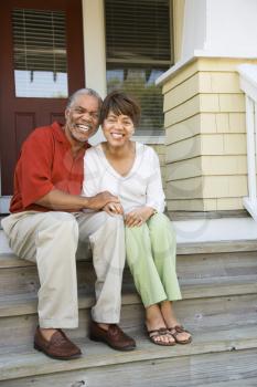 Couple sitting on outdoor steps of home smiling. Vertically framed shot.