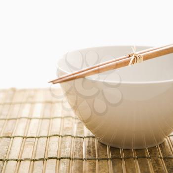 Chopsticks lying across an empty bowl on a bamboo mat. Square format. Isolated on white.