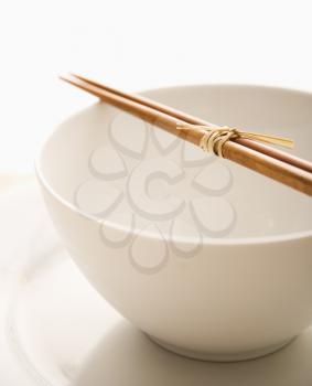 Chopsticks lying across an empty bowl that is on top of a plate. The dishes are white. Vertical shot. Isolated on white.