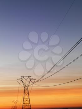 Line of electrical towers and power lines at sunset. Vertical shot.