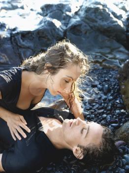 Attractive young woman lies on top of a young man on a rocky coast. Vertical shot.