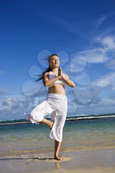 Asian woman standing in a yoga tree pose on Maui Hawaii beach. Vertical shot.