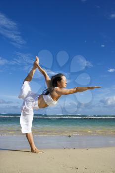 Side view of an Asian woman in a Yoga pose on Maui Hawaii beach with the ocean in the background. Vertical shot.