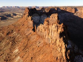 Mesa crag with shadows covering one side. A canyon can be seen in the distance. Horizontal shot.