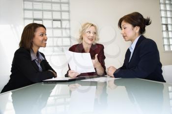 Three businesswomen sitting at office desk having meeting and discussing paperwork.
