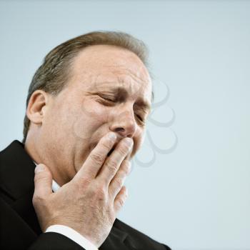 Head and shoulder portrait of middle aged  Caucasian businessman yawning.