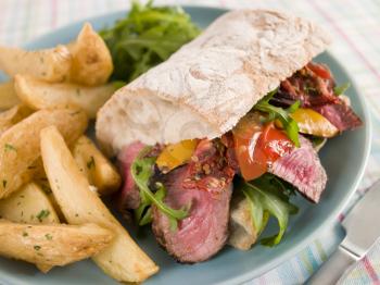 Royalty Free Photo of a Steak and Roasted Pepper Ciabatta Sandwich with Spiced Potato Wedges