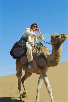 Royalty Free Photo of a Man on a Camel in the Desert With a Cellphone
