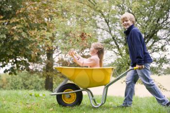 Royalty Free Photo of a Boy Pushing a Girl in a Wheelbarrow